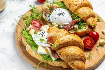 Croissant with prosciutto, poached egg, jamon, blue, cheese, avocado, microgin and cherry tomatoes. Mediterranean appetizer. Breakfast concept
