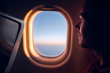 Portrait of man traveling by airplane. Passenger looking through plane window during flight at...