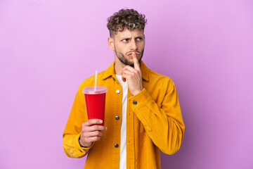 Young blonde man holding soda isolated on purple background having doubts while looking up