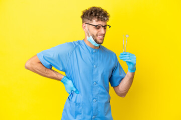 Dentist blonde man holding tools isolated on background suffering from backache for having made an...