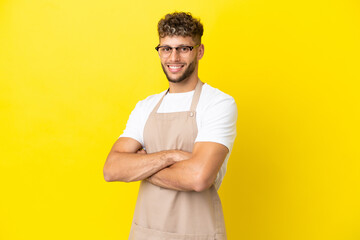 Restaurant waiter blonde man isolated on yellow background with arms crossed and looking forward