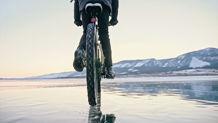 Man is riding bicycle on the ice. Ice of the frozen Lake Baikal. Teenage is dressed in black down...