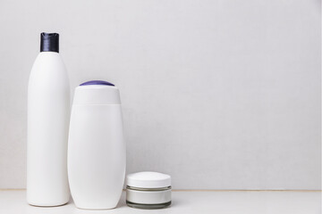 Preparation for hotel spa treatment or home bath procedure. Gray bathroom shelf or table with accessories and cosmetics. Shampoo, shower gel, hair conditioner, soft cream glass bottle with copy space