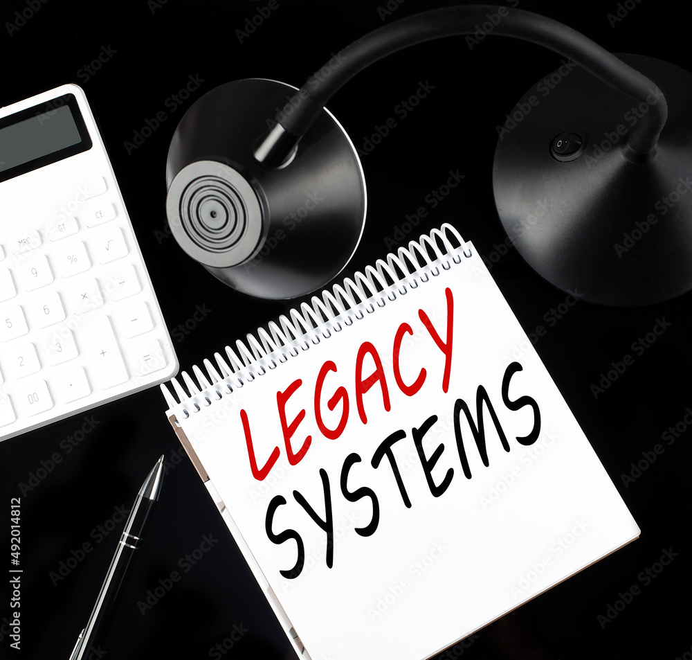 Poster opened paper notebook with text legacy systems with a pen, calculator and table lamp on black backgr