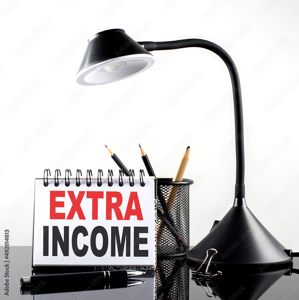 Poster extra income text on notebook with pen and table lamp on the black background