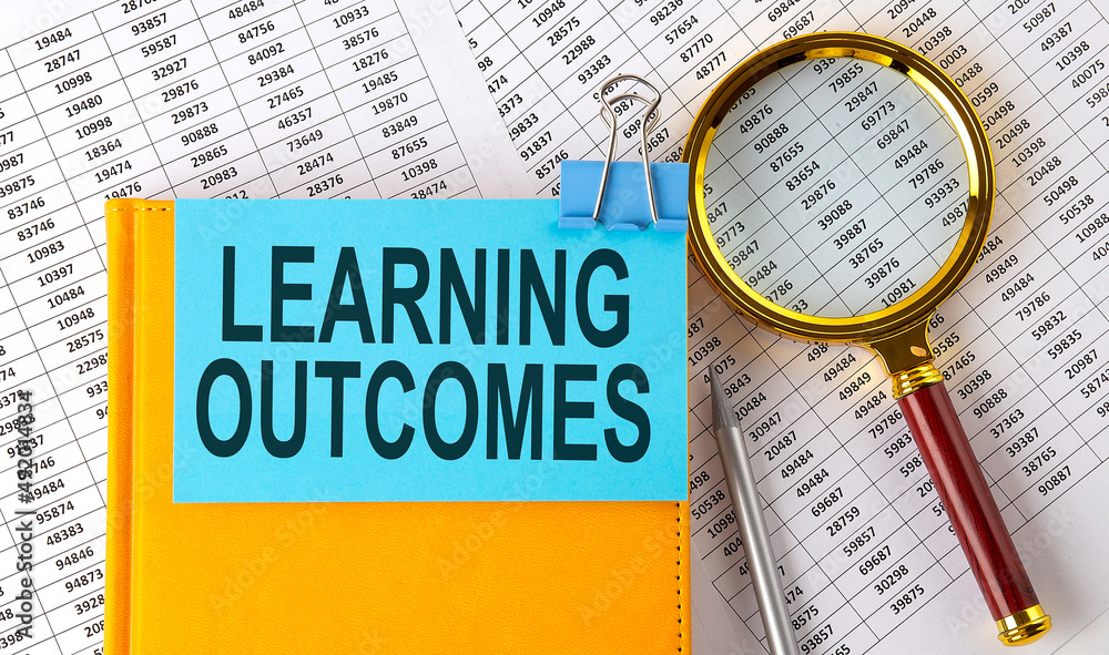 Aufkleber learning outcomes text on sticker on notebook with magnifier and chart. business concept