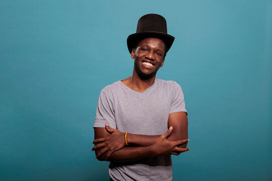 African American Man With Arms Crossed Wearing Top Hat To Create Magical Artistic Performance, Showing Confidence For Vintage Fashion. Young Adult With Theater Prop Costume In Studio.