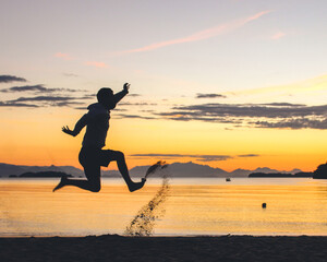 silhueta de homem não identificado pulando na praia durante o nascer do sol 