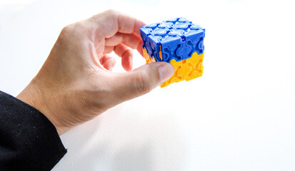 Left Hand holding blue and yellow cube on white background