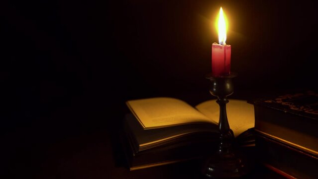 Dark mysterious image of a pewter candlestick with a burning candle stub illuminating an open book