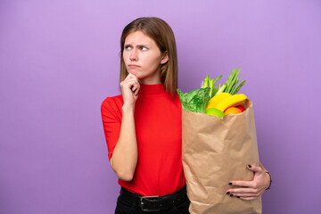 Young English woman holding a grocery shopping bag isolated on purple background having doubts and thinking