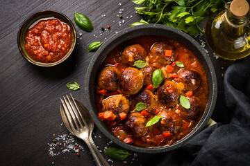 Meatballs in tomato sauce in a skillet on dark wooden table with ingredients. Top view with copy space.