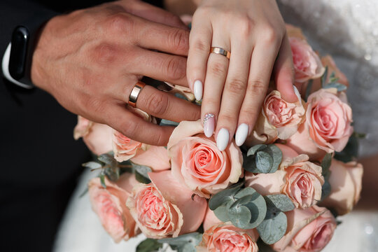hand of a man of the bridegroom and the girl of the bride with gold wedding rings close-up on a wedding bouquet of roses