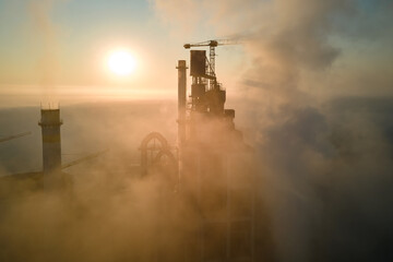 Aerial view of cement factory with high concrete plant structure and tower crane at industrial production site on foggy morning. Manufacture and global industry concept