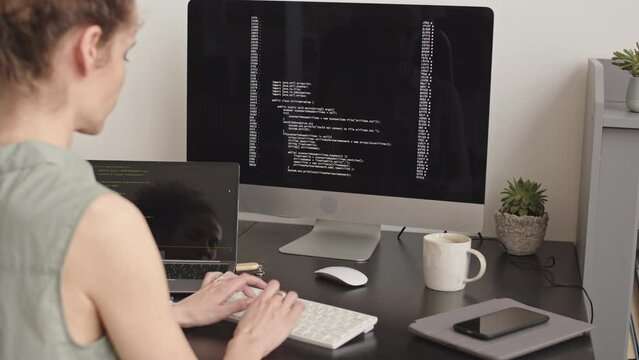 Rear view slowmo of female programmer typing program code on pc computer developing new software in home office
