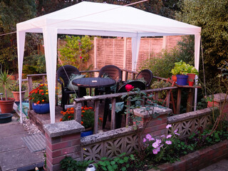 Plastic garden chairs and table under a white plastic gazebo on a small piece of wooden decking