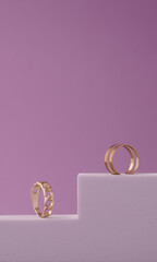 Vertical shot of two modern golden rings on white podium on purple background with copy space