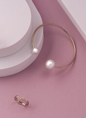 Top view of modern golden and pearls bracelet and ring on pink and white background with copy space