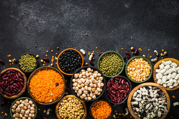 Legumes, lentils, chikpea and beans assortment in different bowls on black stone table. Flat lay image with space for design.