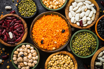 Legumes, lentils, chikpea and beans assortment in different bowls on black stone table. Top view, close up.