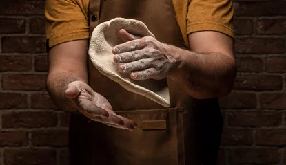 Foto op Canvas flying pizza dough with flour scattering in a freeze motion of a cloud of flour midair on black. Cook hands kneading dough. copy space © Надія Коваль