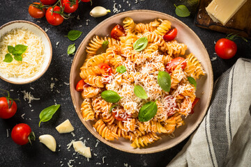 Italian pasta alla arrabiata with basil and parmesan cheese on dark table. Top view with ingredients.