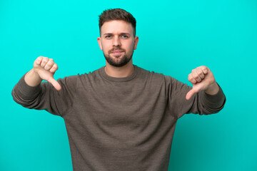 Young caucasian man isolated on blue background showing thumb down with two hands