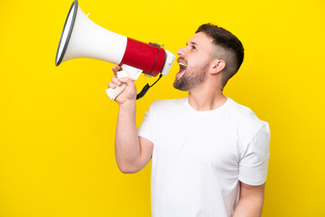 Young caucasian man isolated on yellow background shouting through a megaphone to announce something in lateral position