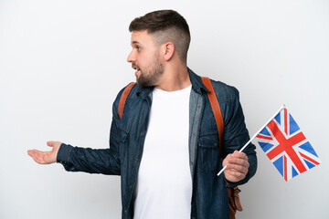 Young caucasian man holding an United Kingdom flag isolated on white background with surprise expression while looking side