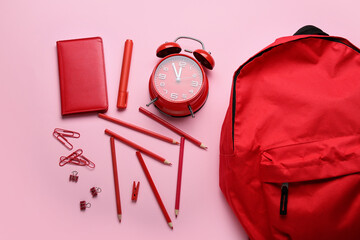 Set of stationery, alarm clock and backpack on pink background