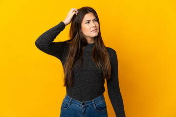 Teenager Brazilian girl isolated on yellow background having doubts while scratching head