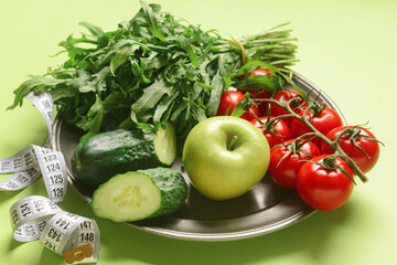 Plate with healthy products and measuring tape on green background, closeup