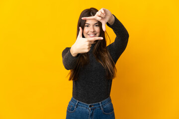 Teenager Brazilian girl isolated on yellow background focusing face. Framing symbol