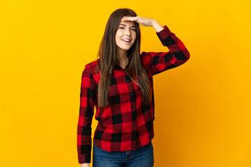 Teenager Brazilian girl isolated on yellow background looking far away with hand to look something