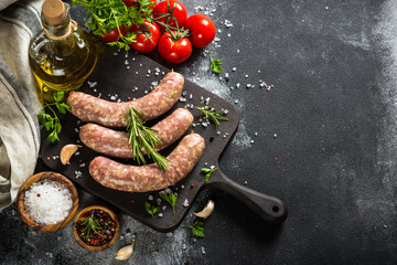 Bratwurst or sausages on cutting board with spices at black table. Top view with copy space.
