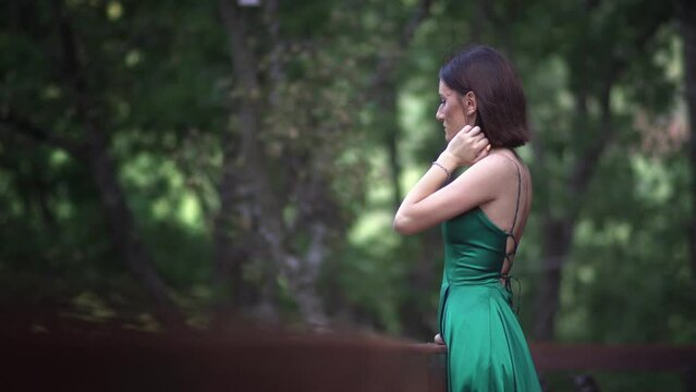 Beautiful young woman in a long green silk dress posing during a photo shooting in the forest.