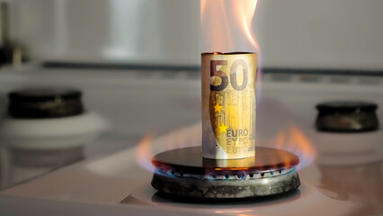 Concept of gas crisis. 50 euro bill is burning on a kitchen stove burner. European cash money. High...