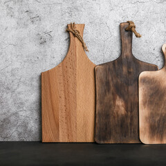 Samples of three different rustic wooden cutting boards on a kitchen countertop against a concrete wall. Manufacture of household goods and accessories made of wood