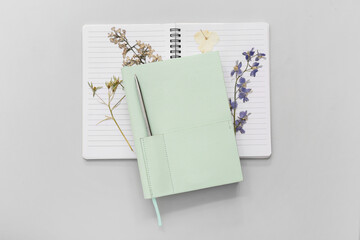 Stylish notebooks with pen and dried flowers on light background