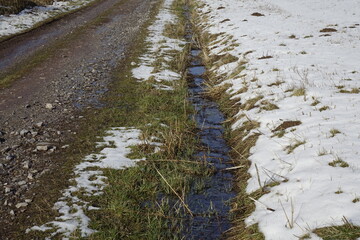 Gravel road, ditch with melting water, snowy meadow in Westerwald, concept: winter, melting, spring (horizontal), Rabenscheid, Hessia, Germany