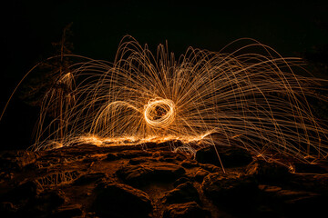 Goldene Funken sprühen nachts bei Steine Felsen Pfütze reflektiert die Funken durch glühende Stahlwolle die im Kreis geschleudert wird, Deutschland