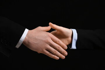 Business colleagues shaking hands on black background, closeup