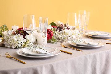 Stylish table setting with wedding invitations and gypsophila flowers near yellow wall