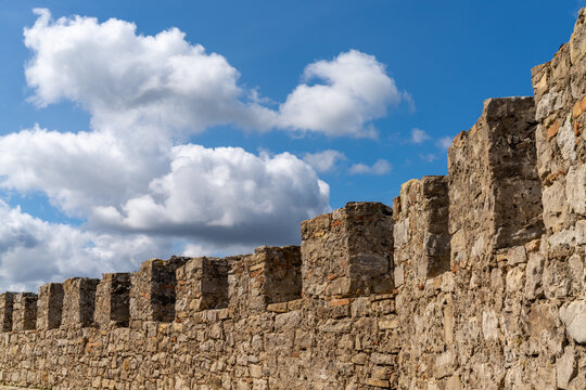curved castle wall and battlements under a blue sky with white cumulus clouds