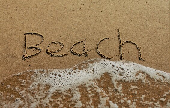 On the beach, the words Beach are carved in letters in the smooth sand, which is washed away by a wave