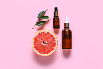 Bottles with essential oil and half of ripe grapefruit on pink background