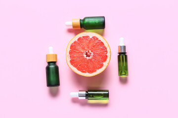 Half of grapefruit and bottles of essential oil on pink background