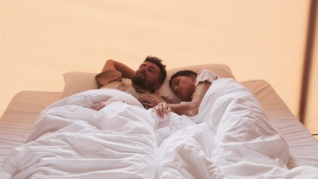 Young Biracial woman and bearded husband sleeping in bed in hotel room in morning