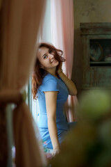 Naklejka premium A girl with red hair is sitting on a window in a room with a vintage interior.