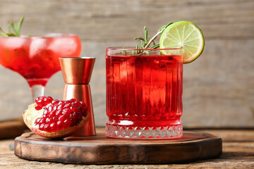 Glass of tasty pomegranate cocktail and measure cup on wooden background